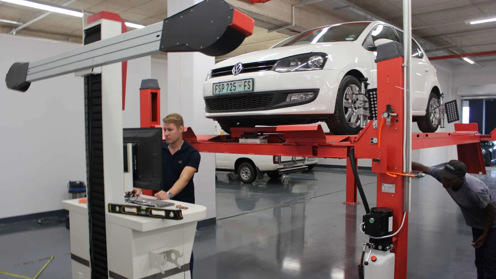 Technicians commissioning wheel-alignment equipment on a four-post lift